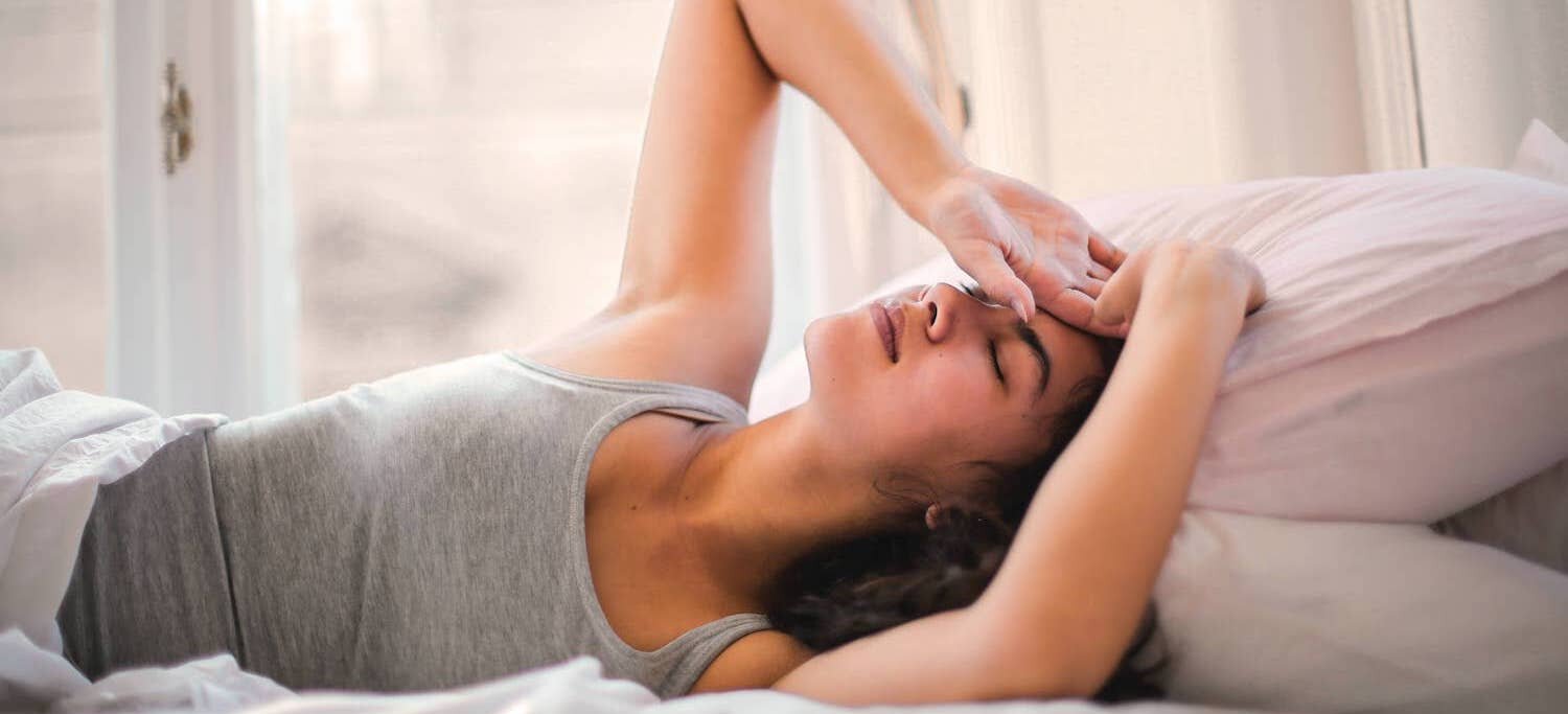 Woman lying in bed grabbing her head in pain due to a headache