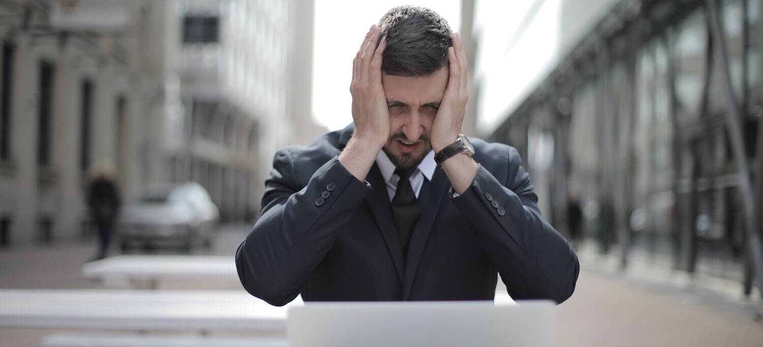 Business man grabbing his face in pain while trying to work