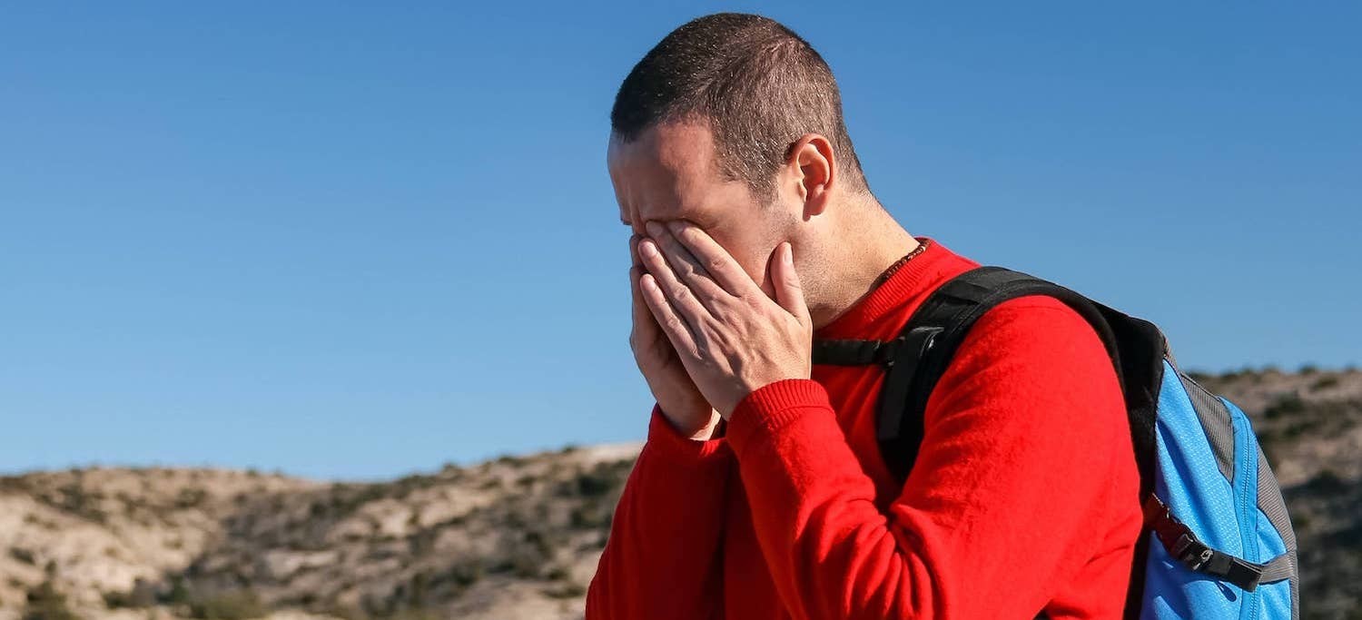 Man grabs his jaw in pain while hiking outside