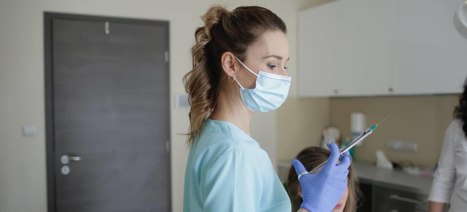 Female Dentist Holding a Needle Preparing for a TMJ Injection- Online Postgraduate Dentisty Degree Training in Orofacial Pain