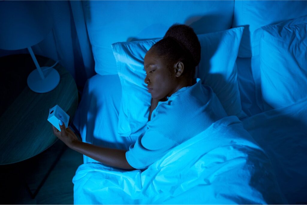 African American woman looking at alarm clock at night laying down in bed because she can't sleep. 