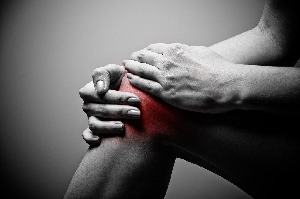 Black and white photo of ands holding a knee and red color around the knee.