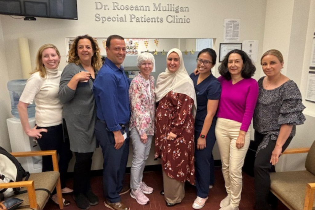 Geriatric Dentistry students and faculty smiling in front of the Special Patients Clinic sign.